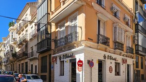 Une vue de rue avec un immeuble dont la façade est blanche, qui possède plusieurs balcons et sur lequel on peut lire l’inscription « Café et restaurant ».