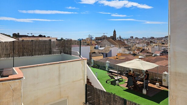 Une terrasse sur le toit offrant une vue sur le paysage urbain, avec notamment une tour imposante et des grues de construction.