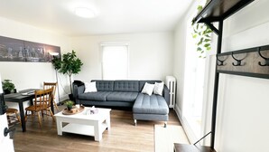 Una sala de estar moderna con un sofá seccional gris, una mesa de centro blanca y un comedor con una mesa y sillas de madera.