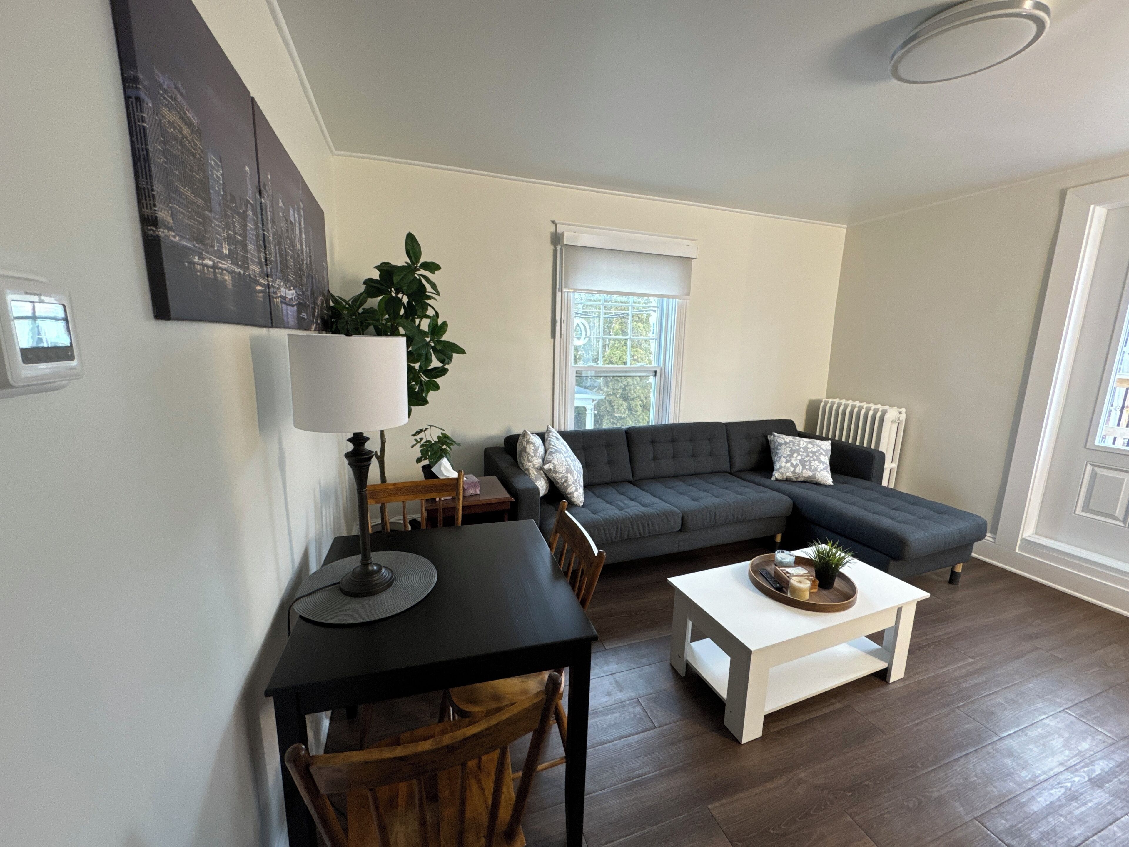 Ein modernes Wohnzimmer mit einem dunkelgrauen Sofa, einem weißen Couchtisch, einem schwarzen Tisch mit Lampe und einem Holzstuhl.