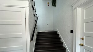 Una escalera con peldaños oscuros que conduce a una plataforma, flanqueada por puertas blancas con pomo de latón.