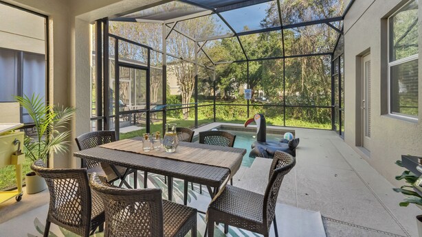 An outdoor patio with a pool, wicker furniture, and a view of the surrounding greenery. - 5BD - Movie Room, Pool, BBQ - Near Disney World (Kissimmee)