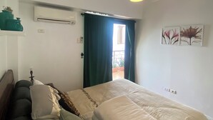 Un dormitorio con cama, mesita de noche, lámpara colgante, ventana con cortinas y aire acondicionado instalado en la pared.