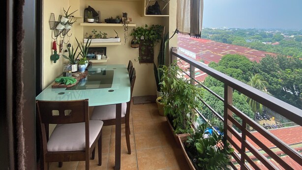 Un balcón con una mesa y sillas, plantas en macetas y una cesta colgante.