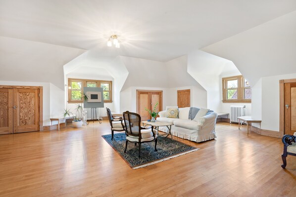 A spacious loft with high ceilings, wooden floors, and a cozy seating area with a white sofa and chairs.