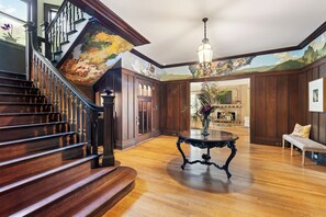A grand staircase with a wooden finish, a round table with a vase, and a mural on the ceiling.