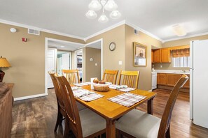 A dining area with a wooden table and chairs, a kitchen in the background, and a clock on the wall. - 2BD 2BA|Indoor Pool and Hot Tub| Handicap Accessible Bath| Sleeps 6 (Pigeon Forge)