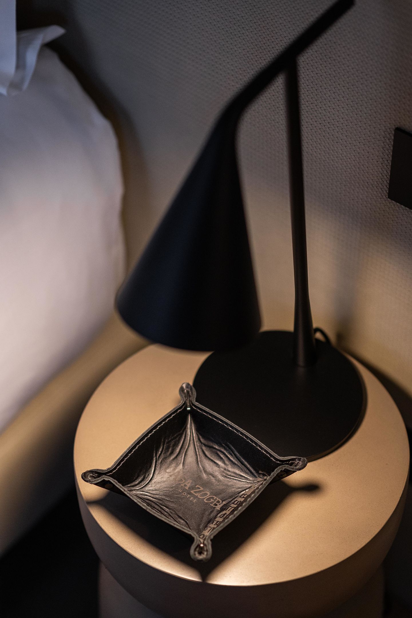 Una mesita redonda con una lámpara negra y un bolso negro encima.