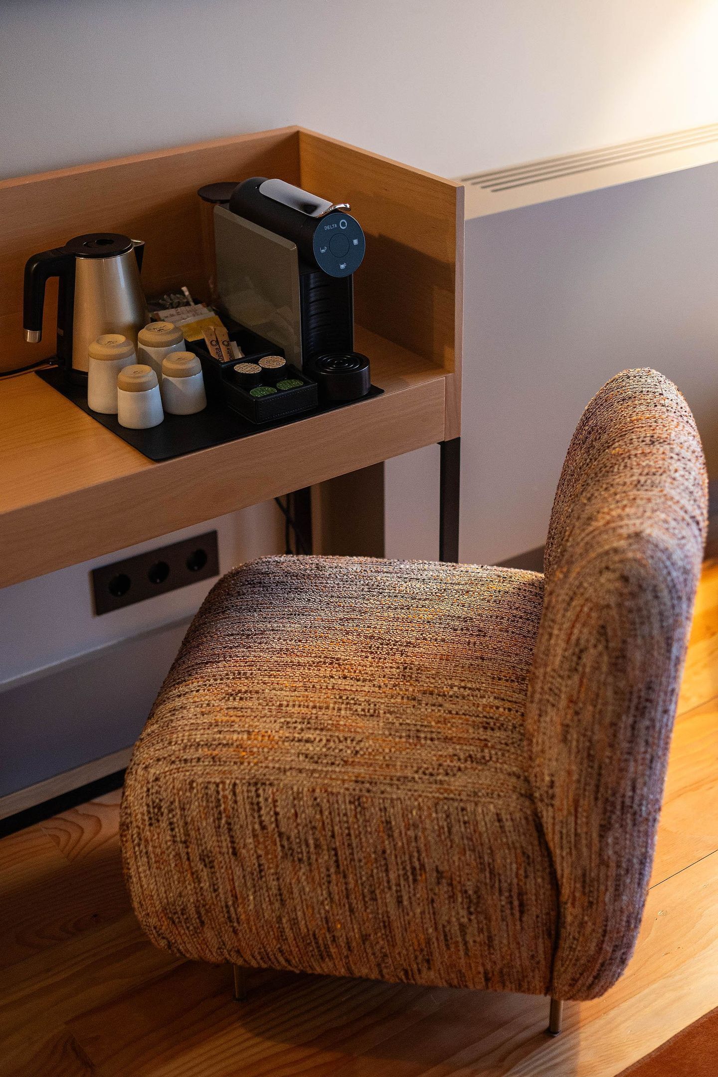 A cozy room with a wooden desk, a coffee machine, and a woven chair.