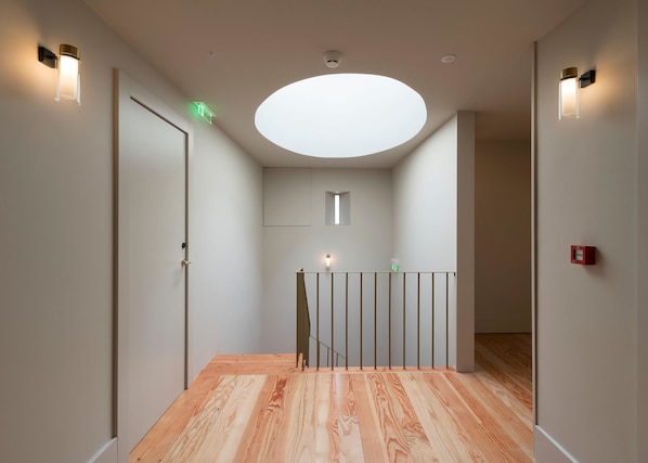 A modern hallway with a wooden floor, a glass railing, and recessed ceiling lighting. - Casa Zogbi hotel (Porto)