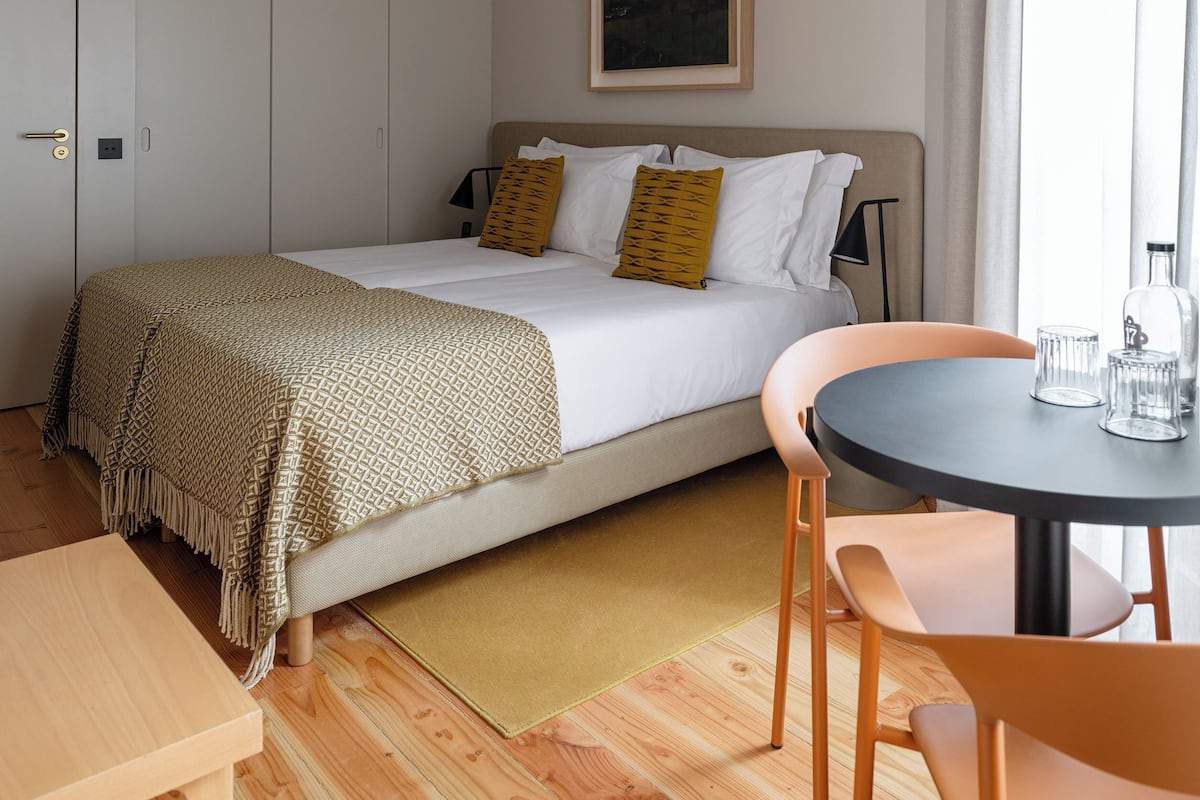 A bedroom with a bed, a bedside table, a chair, a small table, and a painting on the wall.