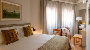A bedroom with a bed, a desk, and a chair. There is a painting on the wall and a window with curtains. - Casa Zogbi hotel (Porto)