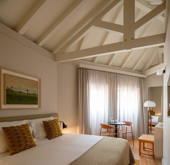 Ein Schlafzimmer mit Bett, Schreibtisch und Stuhl. An der Wand hängt ein Gemälde und das Fenster ist mit Vorhängen dekoriert.