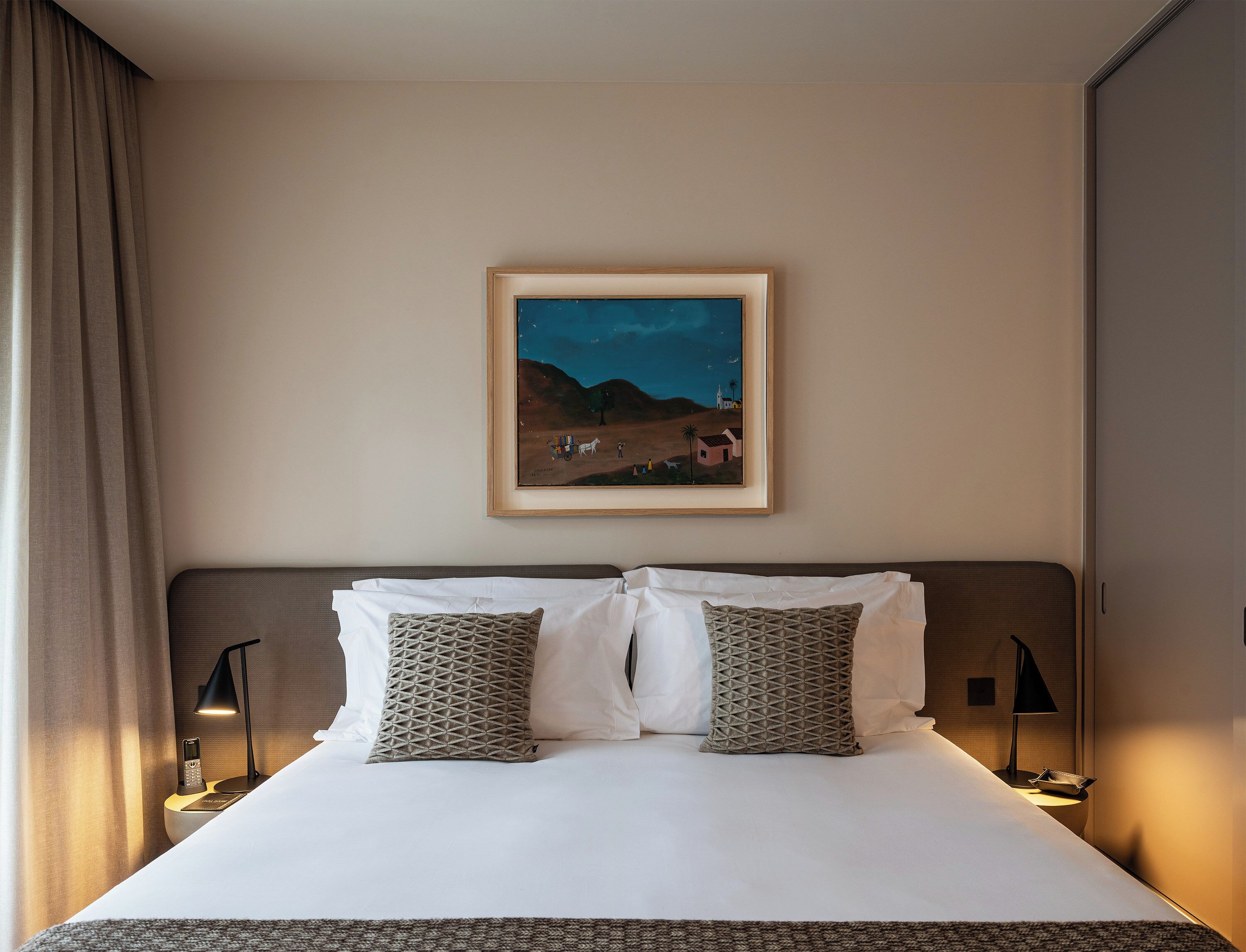 A neatly made bed with two pillows, a framed painting above it, and bedside lamps.