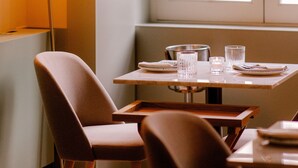 A dining area with a table set for two, a tall floor lamp, and a window with a view of buildings. - Casa Zogbi hotel (Porto)
