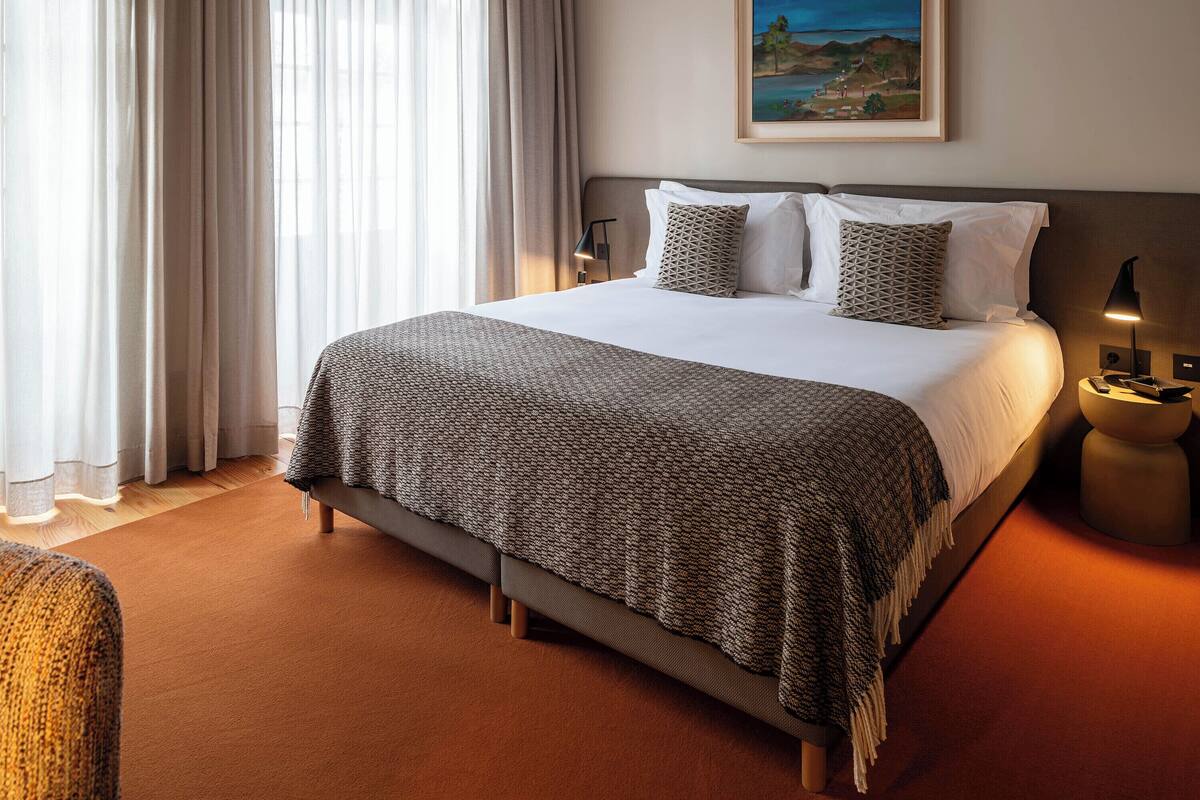 A hotel room with a large bed, a painting on the wall, and a nightstand with a lamp.