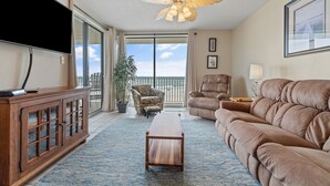 A living room with a TV, wooden cabinet, sofa, and ceiling fan. - 🏝️Beachfront-Spacious Balcony-Pool-Romar Place 305🏝️ (Orange Beach)