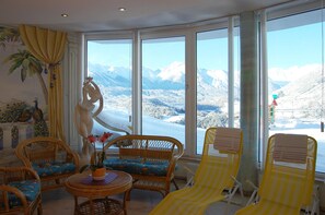 A room with large windows offering a mountain view, wicker furniture, and a statue. - Apartment in Pitztal With Mountain Views (Arzl im Piztal)