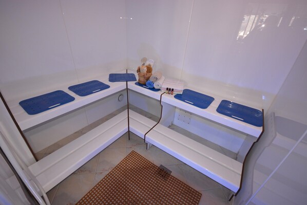 A corner bathroom with white tiled walls, a brown mat, and blue mats on the counters. - Apartment in Pitztal With Mountain Views (Arzl im Piztal)