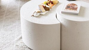Un pouf rond et blanc, sur lequel sont posés un plateau de collations et un livre.