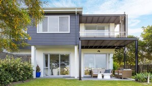 Une maison moderne à deux étages, dotée d’un balcon, de grandes fenêtres et d’un jardin bien entretenu.