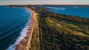 Une vue aérienne d’une zone côtière comprenant une plage, une zone boisée et une côte lointaine.