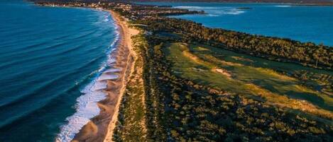 An aerial view of a coastal area with a beach, forested land, and a distant shoreline.