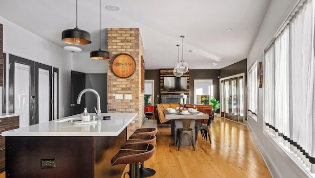 Una cocina moderna con una isla central, taburetes de bar, iluminación colgante y una pared decorada con ladrillos.