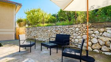 Un espace extérieur aménagé en terrasse, avec des meubles en osier, un mur en pierre et un grand parasol.