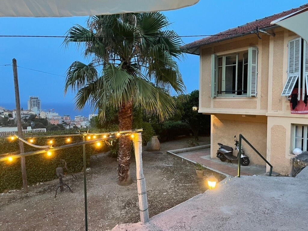 Une maison avec un palmier, un scooter et des guirlandes lumineuses.