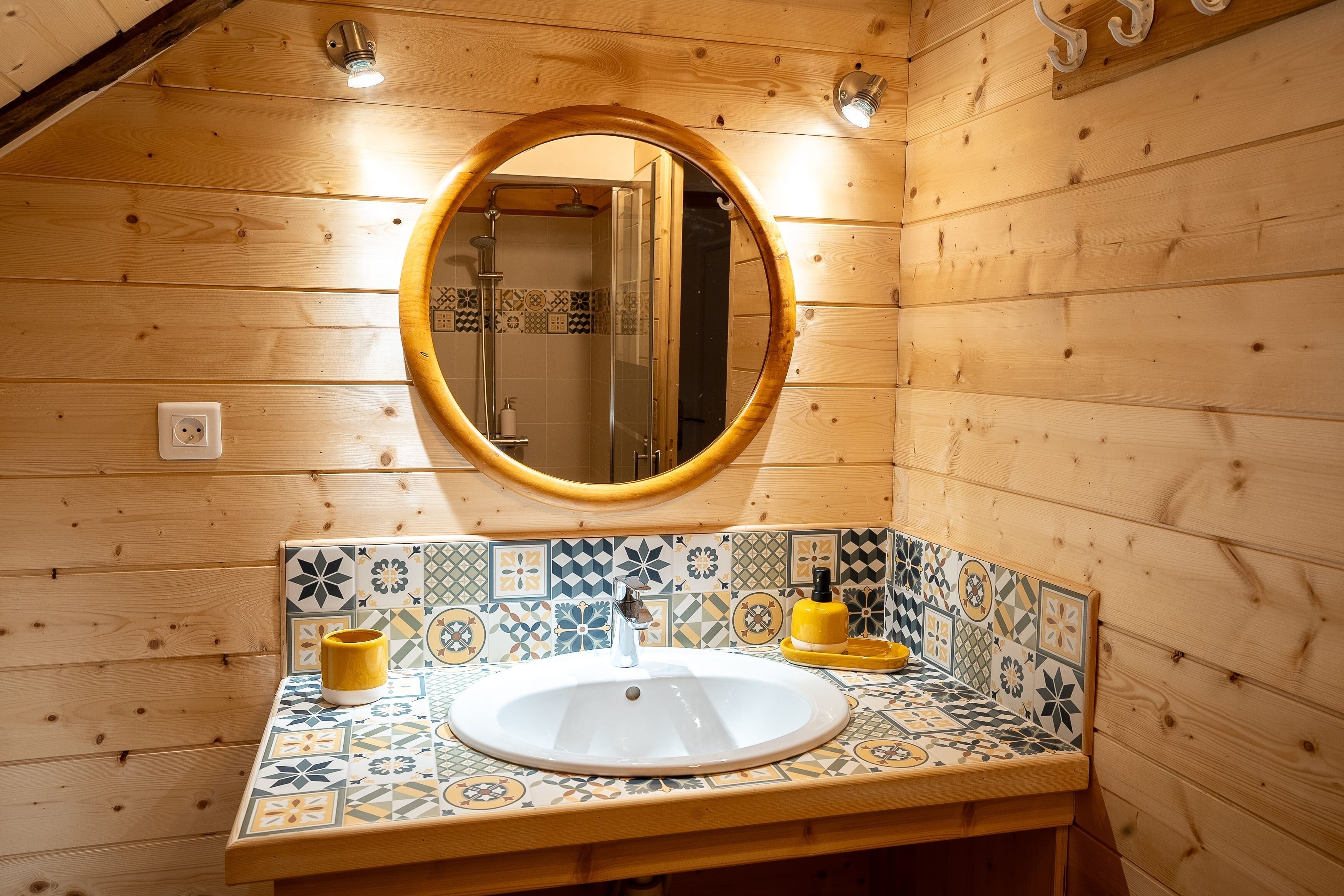 A wooden cabin bathroom with a round mirror, a sink, and a tiled backsplash.