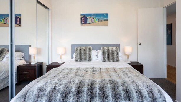 A modern bedroom with a large bed, two bedside tables, a mirror, and a painting on the wall. - Stunning Views Central Apt (Auckland)