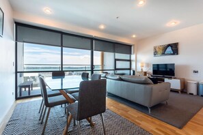 A modern living room with a large window, a sofa, a TV, and a dining area.