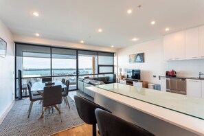 A modern kitchen with a large island, a dining area with a view, and a spacious living area with a large window overlooking a body of water.