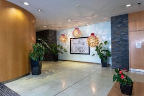 A lobby with a curved wooden wall, a stone accent wall, a framed artwork, and three hanging spherical lamps.