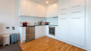 A modern kitchen with white cabinets, stainless steel appliances, and a wooden floor. - Stunning Views Central Apt (Auckland)