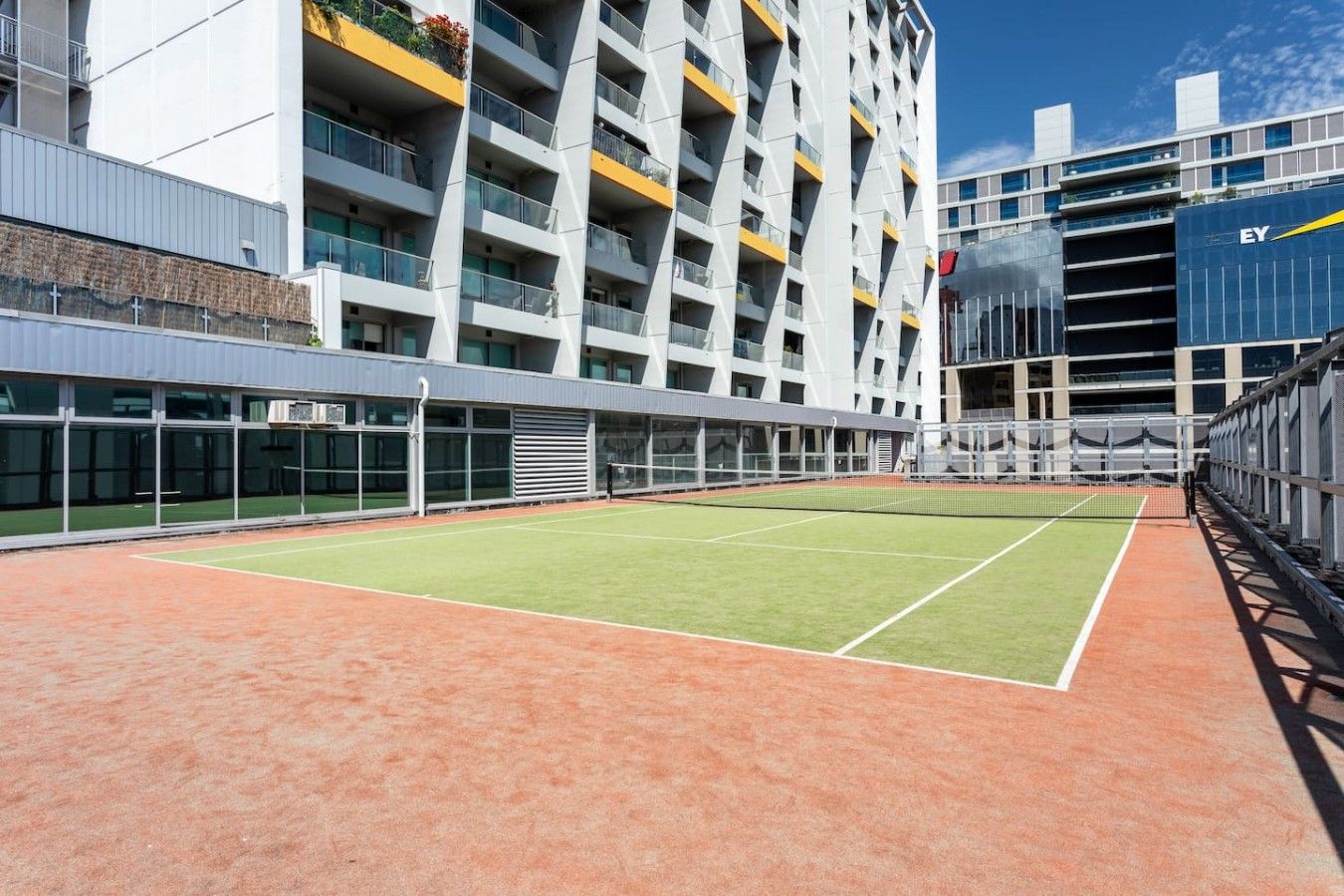 A tennis court adjacent to a modern building with multiple balconies and a glass facade.