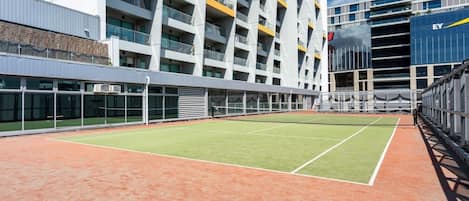 A tennis court adjacent to a modern building with multiple balconies and a glass facade.