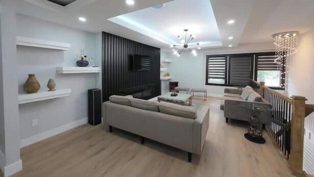 A modern living room with a sofa, a dining area, and a TV mounted on the wall.
