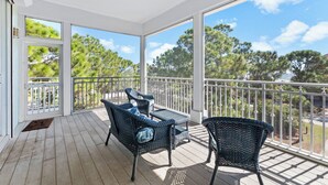 A covered outdoor area with wicker furniture and a view of trees.