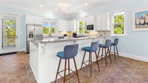A modern kitchen with white cabinets, a large island with bar stools, and a view of greenery outside.