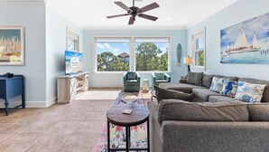 A spacious living room with a ceiling fan, large windows, and a view of the outdoors.