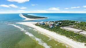An aerial view of a coastal area with a beach, a pier, and a cluster of houses.