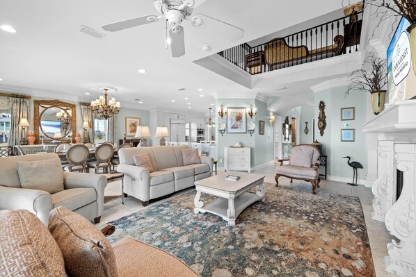 A spacious living room with a high ceiling, a chandelier, and a fireplace. - Luxury By the Sea: Gorgeous Beachfront Home, Private Pool, Amazing Views (Mexico Beach)