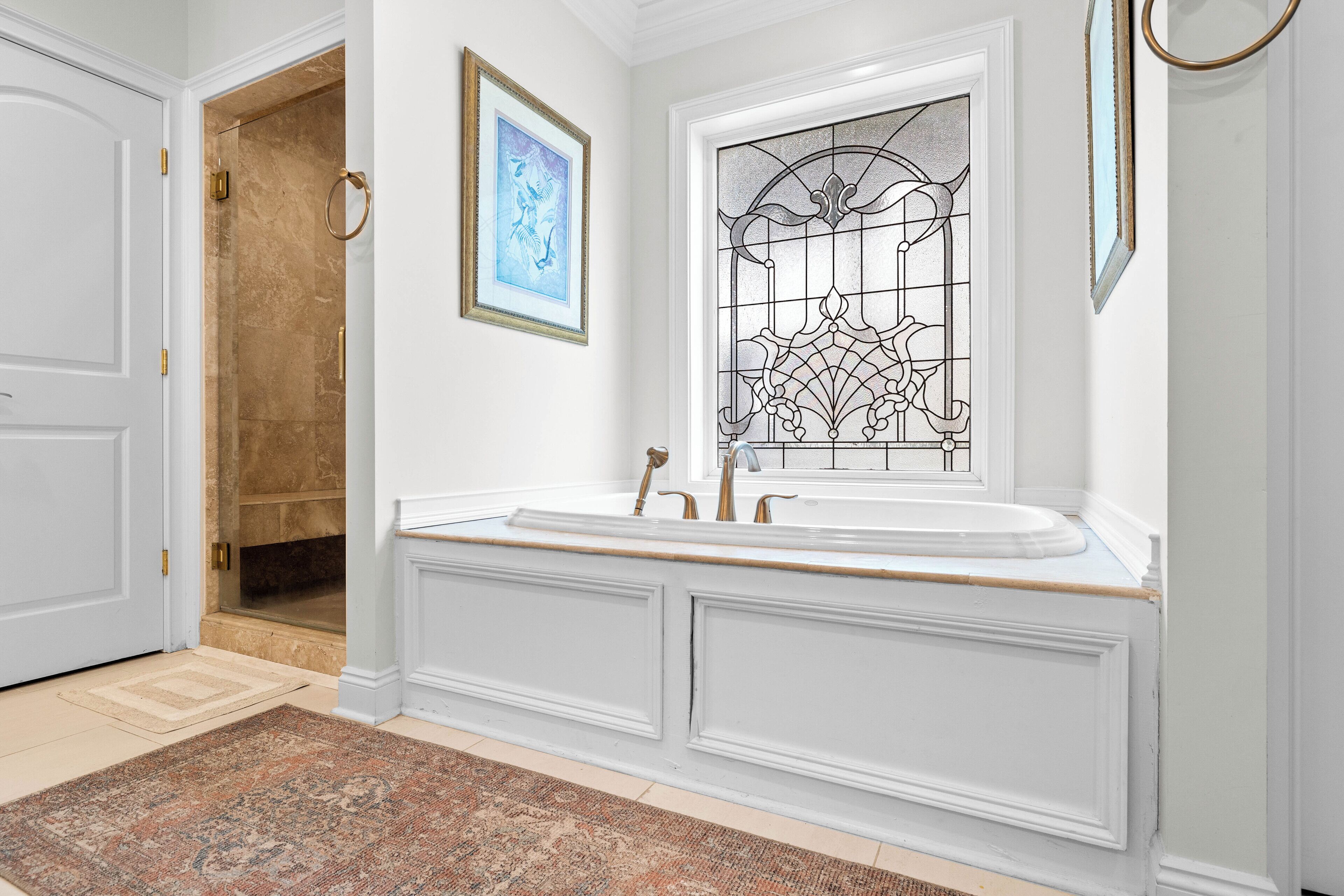 Une salle de bain avec une grande baignoire, une fenêtre ornée de vitraux et un tableau encadré accroché au mur.