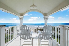 A balcony with two Adirondack chairs, a white table, and a view of the ocean. - Luxury By the Sea: Gorgeous Beachfront Home, Private Pool, Amazing Views (Mexico Beach)