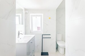 A modern bathroom with a white marble sink, a black towel rack, and a toilet.