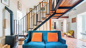 A living room with a blue sofa, a wooden staircase, and a black fireplace. - Casalinho de Bicesse (Cascais)