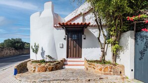A white building with a brown door, stone steps, and a small garden area. - Casalinho de Bicesse (Cascais)