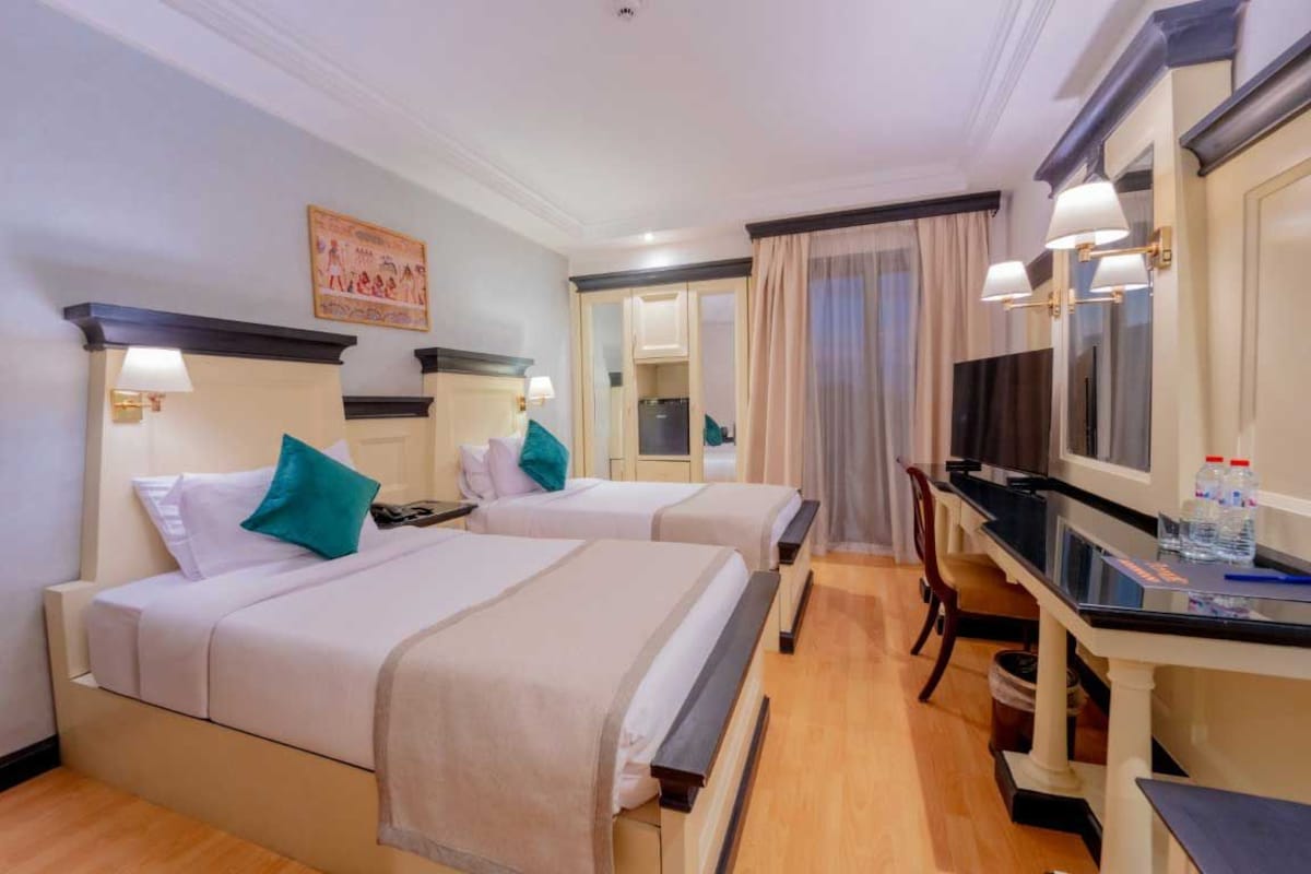 A hotel room with two beds, a desk, a television, and a mirror.